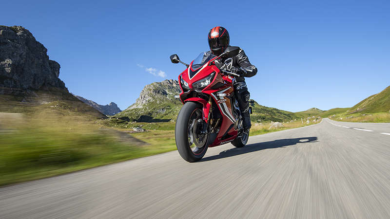 CBR650R, lateral delantero izquierdo de tres cuartos, conducida por un piloto en una carretera de montaña