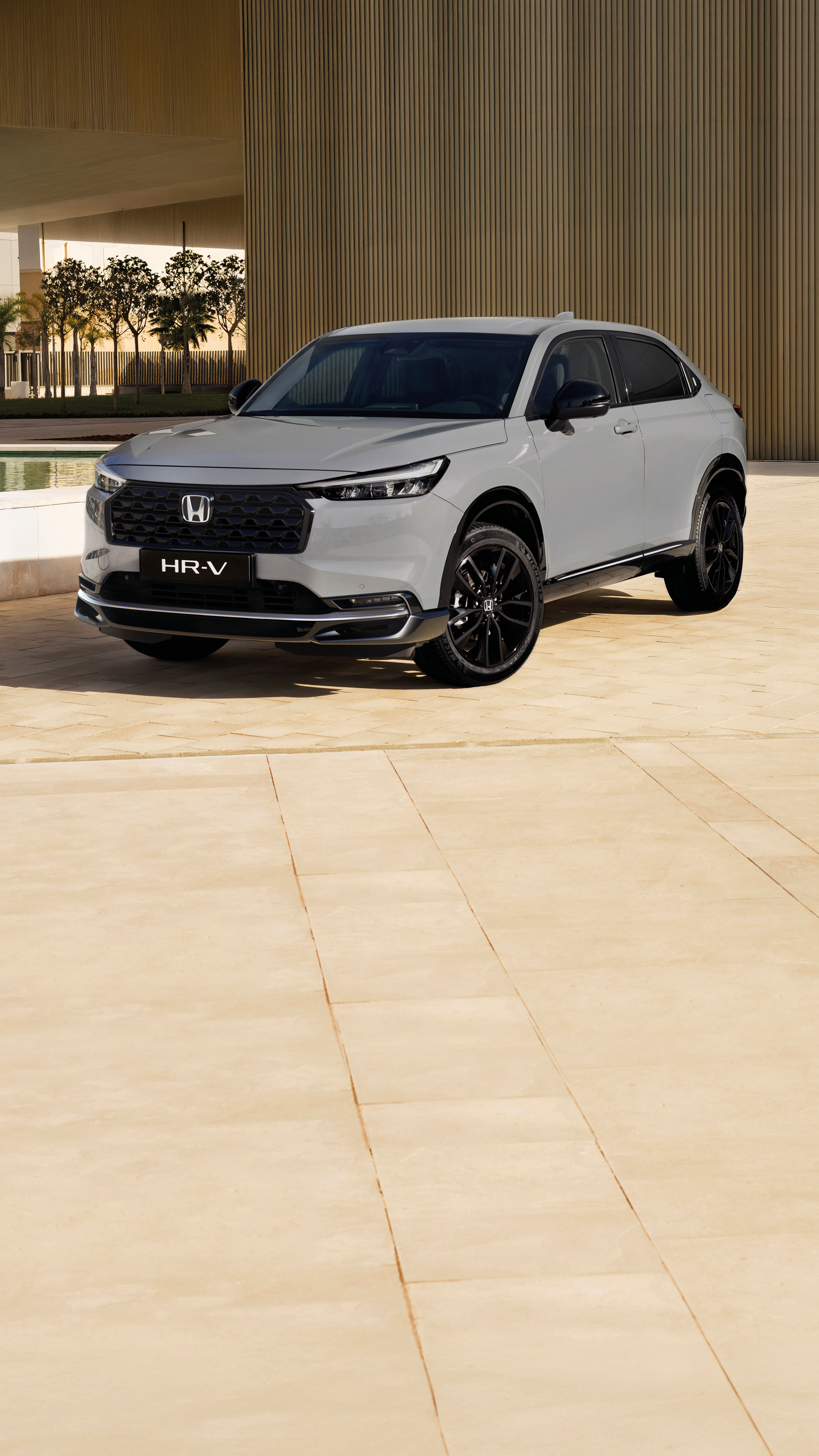 Un SUV Honda HR-V blanco estacionado frente a un edificio moderno con paredes alicatadas en beige. El vehículo está posicionado en ángulo, mostrando su diseño estilizado y su distintiva parrilla delantera.