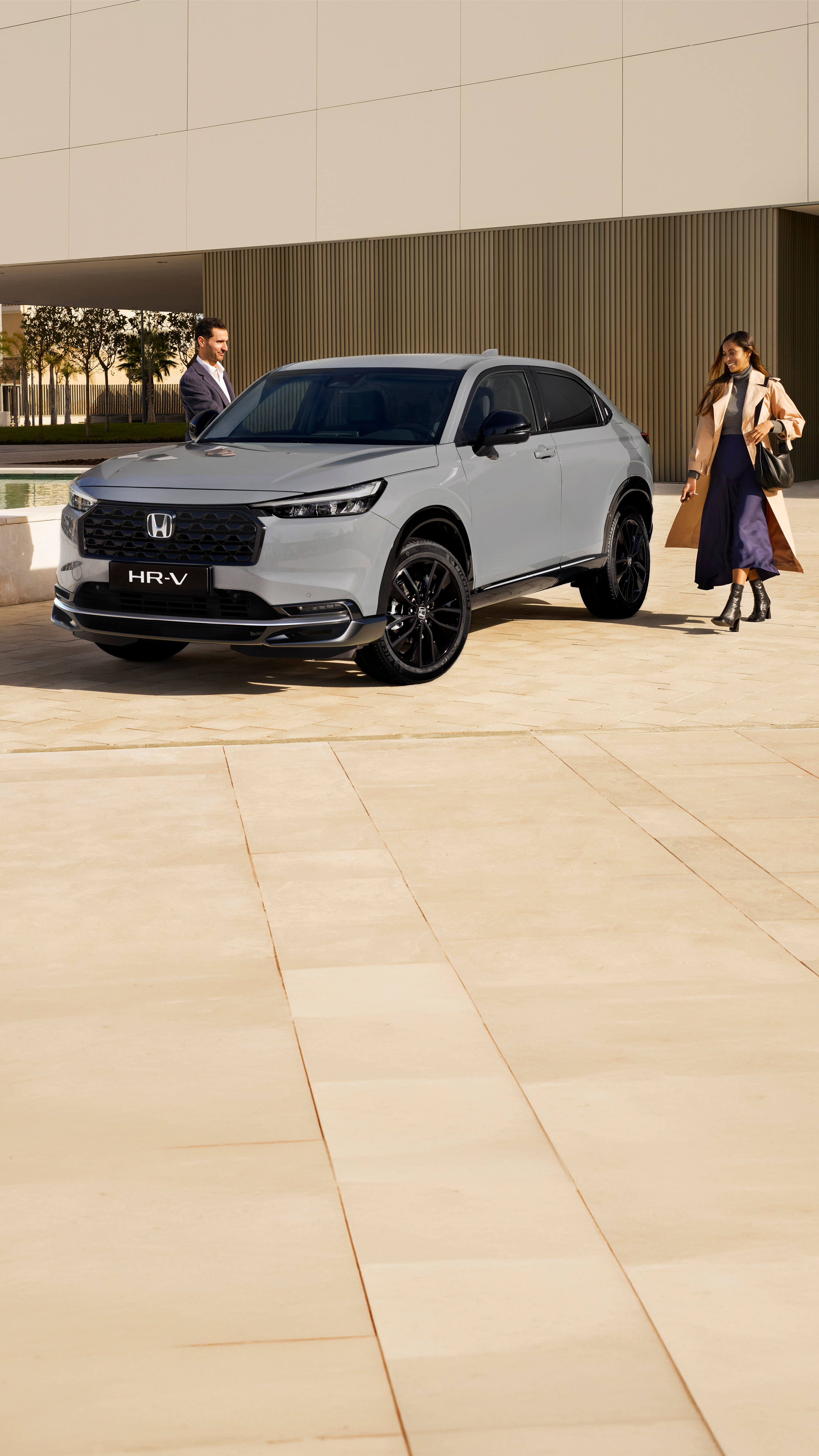 Un SUV Honda HR-V blanco estacionado frente a un edificio moderno con paredes alicatadas en beige. El vehículo está posicionado en ángulo, mostrando su diseño estilizado y su distintiva parrilla delantera.
