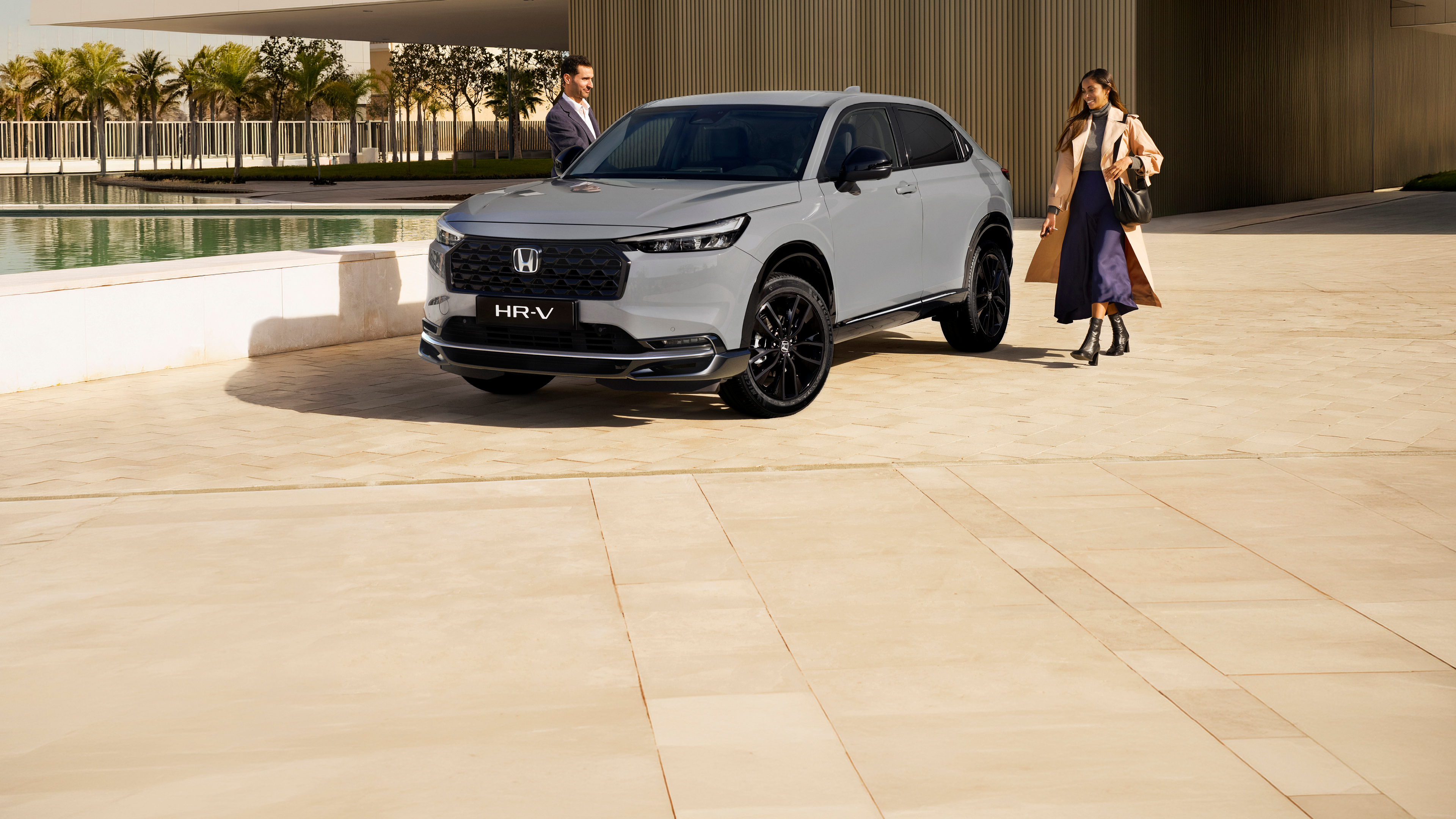 Dos SUV Honda HR-V estacionados frente a un edificio moderno. El HR-V blanco está en primer plano mirando hacia adelante, mientras que el HR-V plateado está al fondo de espaldas, mostrando el diseño frontal y trasero del vehículo.