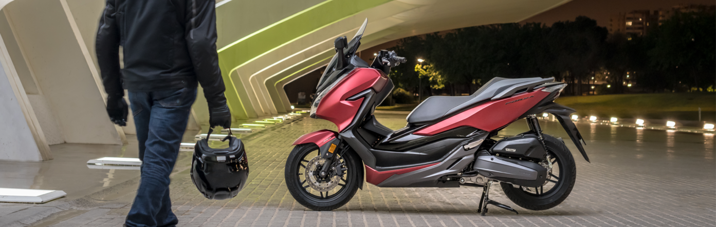 Vista lareral de una Forza 125 roja en el caballete, de noche.